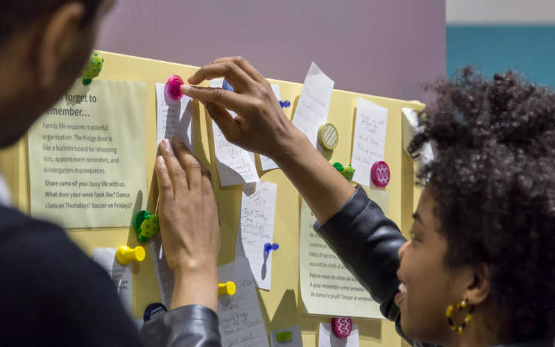 Two people do an activity involving posting pieces of paper with writing on a board.