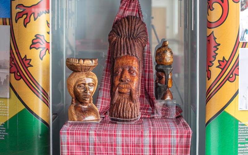 Three Jamaican wooden artifacts sit in a glass display case.