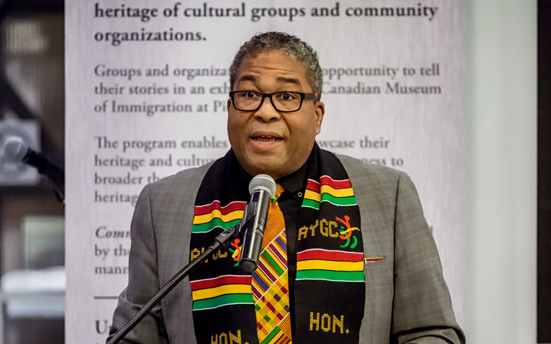 A person wearing a Jamaican scarf speaks into a microphone.