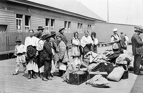 Old black & White photo of beautifully-dressed Ukrainian immigrants with luggage bags and they wait for something.