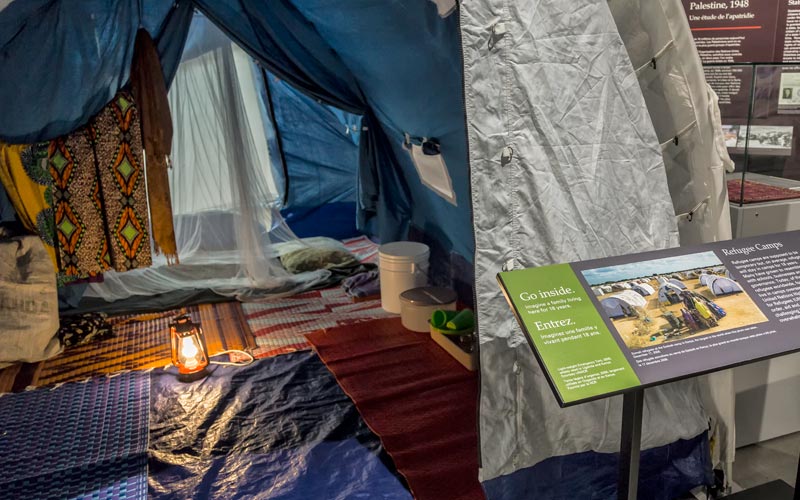 A tent that would be used by refugee camps, with an exhibition panel that says “Go inside.”