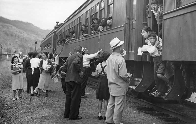 Archival image showing several people on the ground outside a train, while people on the train look out the windows at them.