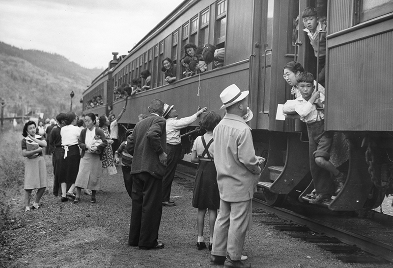 Archival image showing several people on the ground outside a train, while people on the train look out the windows at them.