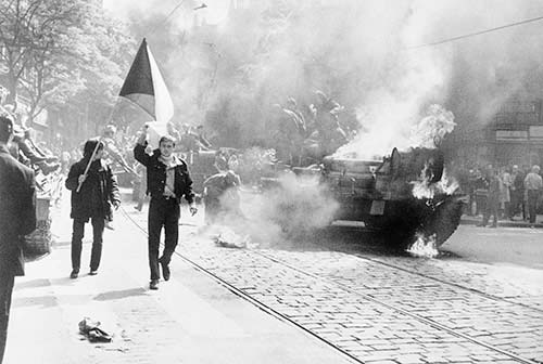 Tanks in the street and people walking and holding a flag
