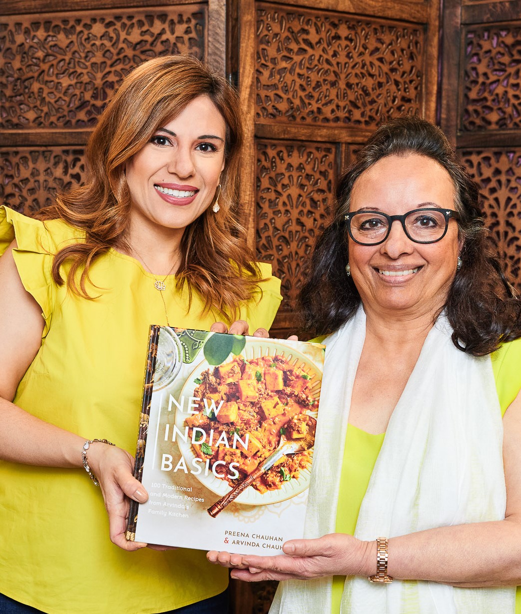 A portrait of two smiling Indian woman holding a copy of their Indian cookbook.