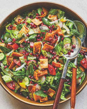 A salad in a brown serving bowl, including lettuce, various vegetables, and pieces of fried pita.