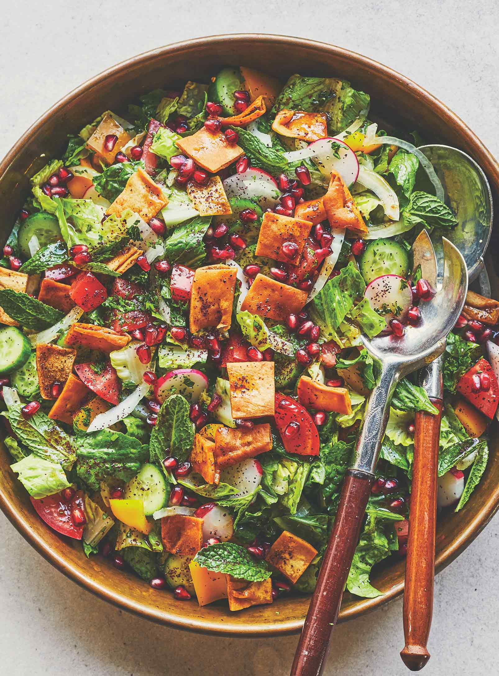 A salad in a brown serving bowl, including lettuce, various vegetables, and pieces of fried pita.