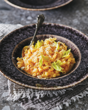 Various shaped pasta and cubed potatoes with sauce in a black bowl, garnished with parmesan cheese.