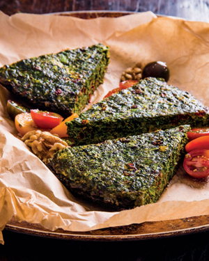 Three pieces of kookoo sabzi served on a plate with parchment paper, sitting on a wooden table.