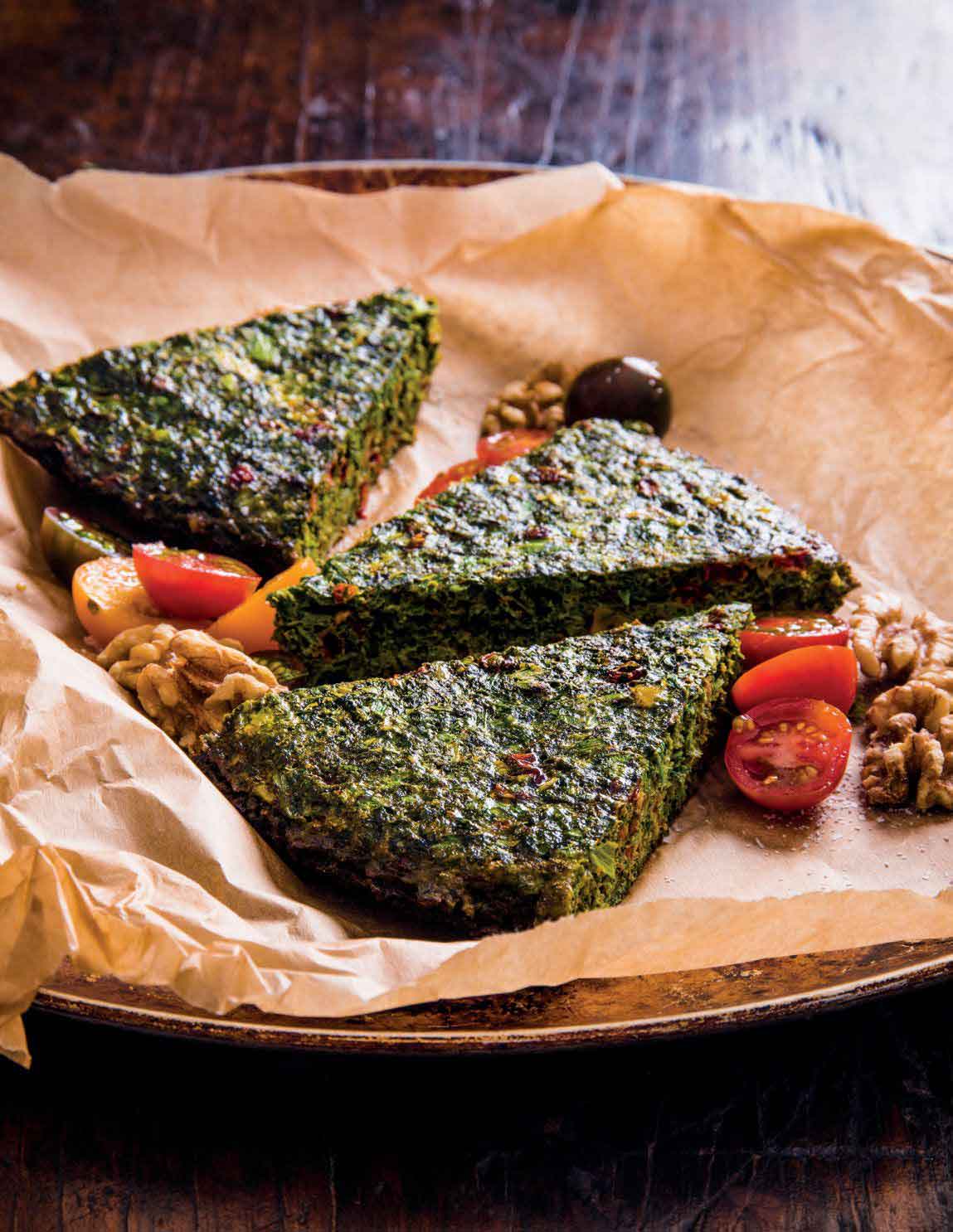 Three pieces of kookoo sabzi served on a plate with parchment paper, sitting on a wooden table.