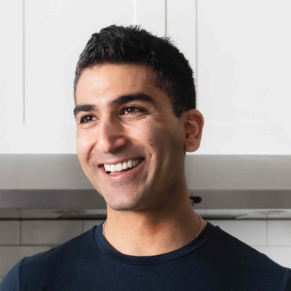 A smiling young man of Egyptian descent folding dough in a bright, white kitchen.