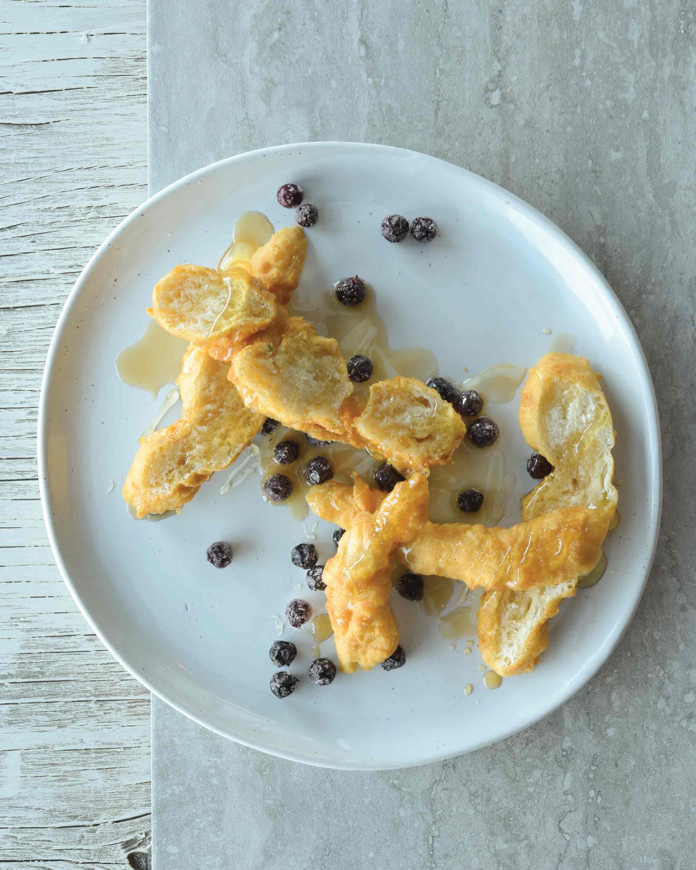 Bannock on a white plate, garnished with berries and syrup.