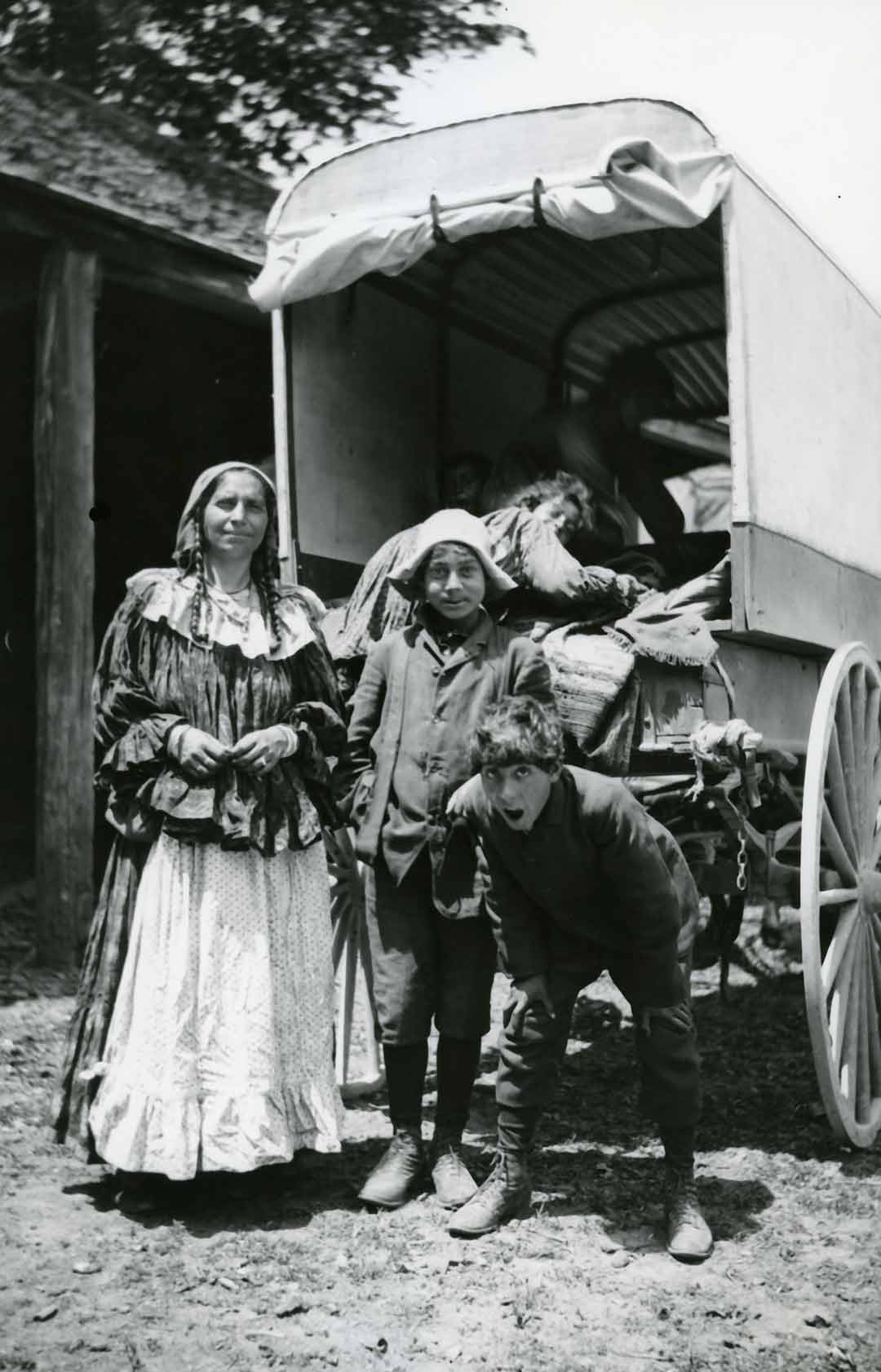 Black-and-white photograph of a woman and two children smiling in front of a caravan.