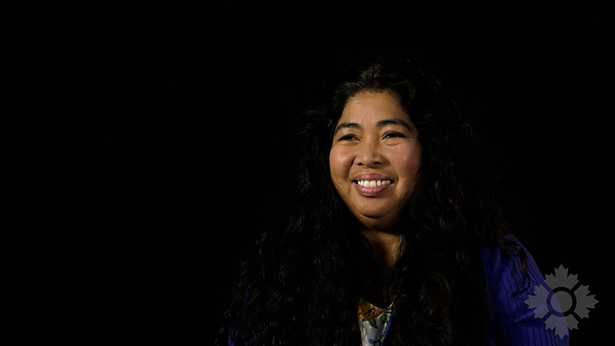 A woman smiles at the camera in front of a black background.