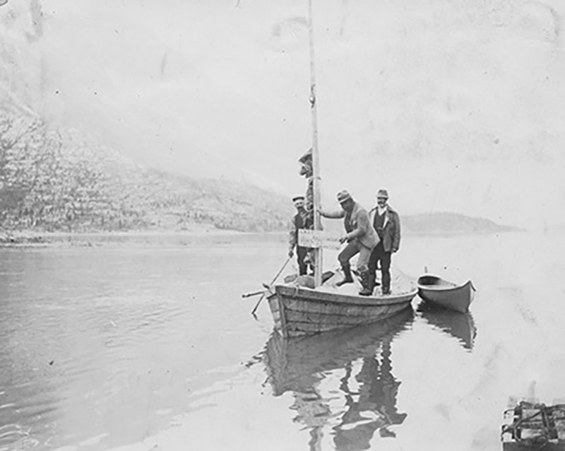 Three men are standing in a boat and there is a small boat in the water next to it.