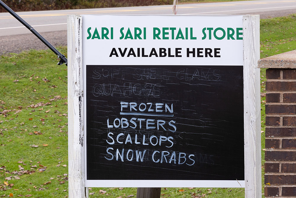 An outdoor sign on wooden posts for the Sari Sari Retail Store advertising available seafood.