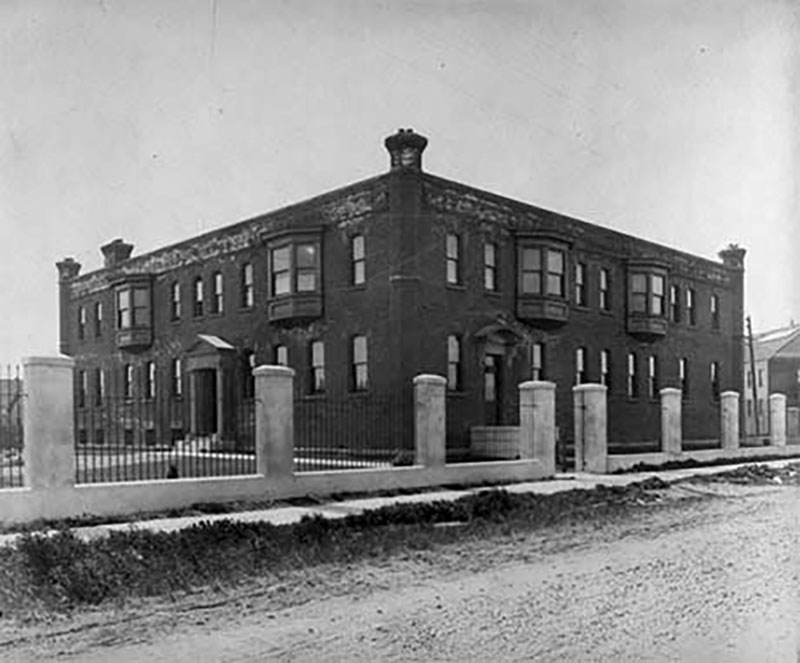 A large building sits behind a gated fence, as seen from across the road.