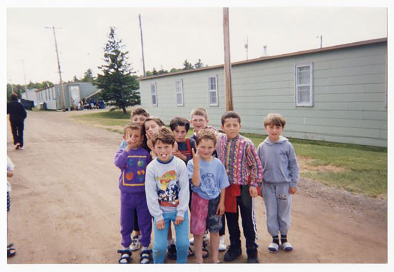 A group of children stand together on a dirt road.