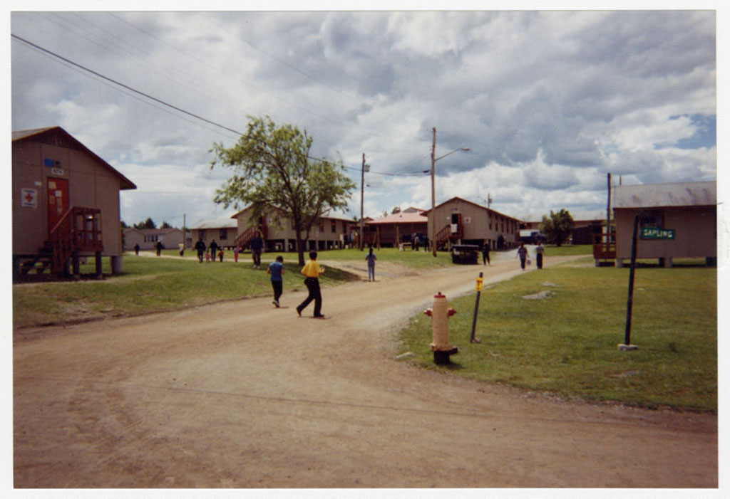 Several buildings around a dirt road with two people walking along the road.