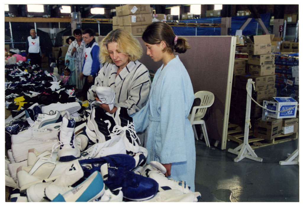 Two women look at shoes from a long table piled with shoes.