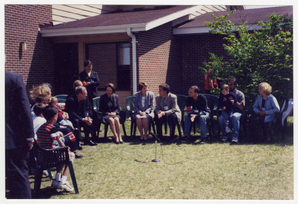 A group of people are seated outside on lawn chairs in a semi circle.