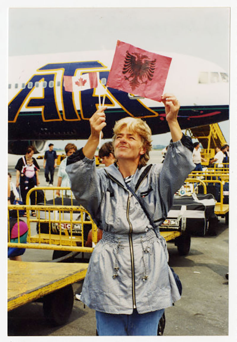 A woman holds a square red paper with a black emblem, behind her is an airplane.