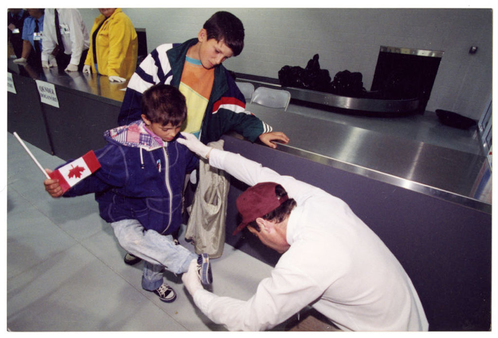 A man is looking at the bottom of a boy's shoes.