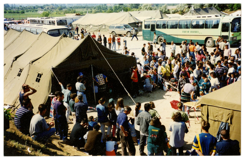 A large crowd of people around a large green tent and a bus.