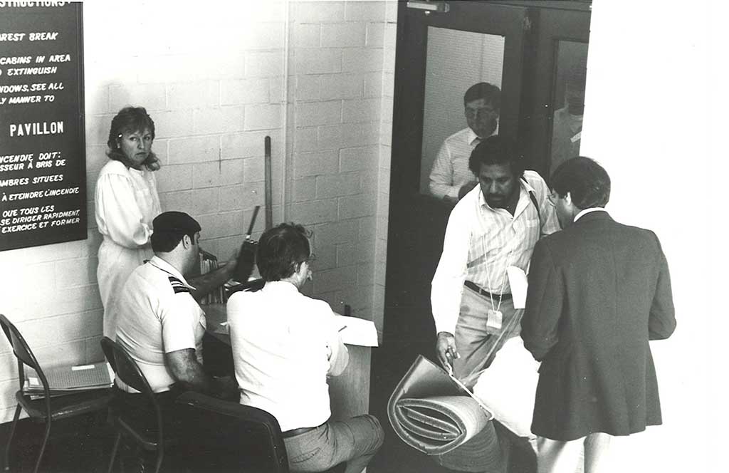 Men and women are crowded around a small desk.