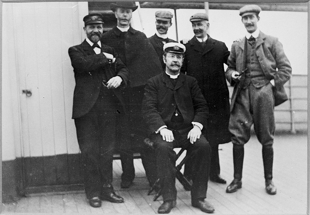 Archival image of six sea captains on the deck of a ship.