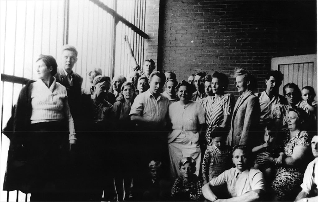 A group of people are standing and sitting near barred windows.