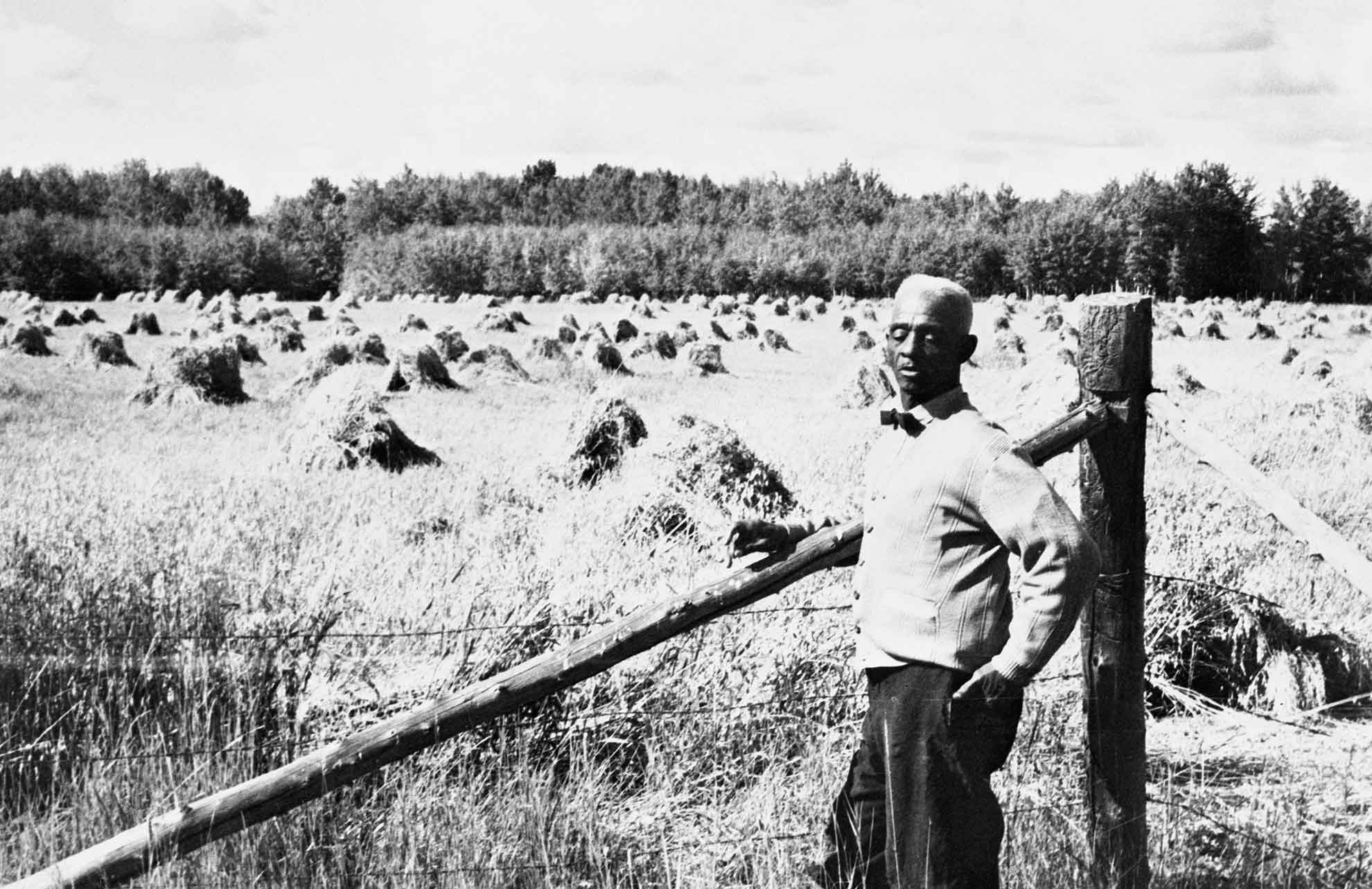 A man stands against a fence in front of a field.