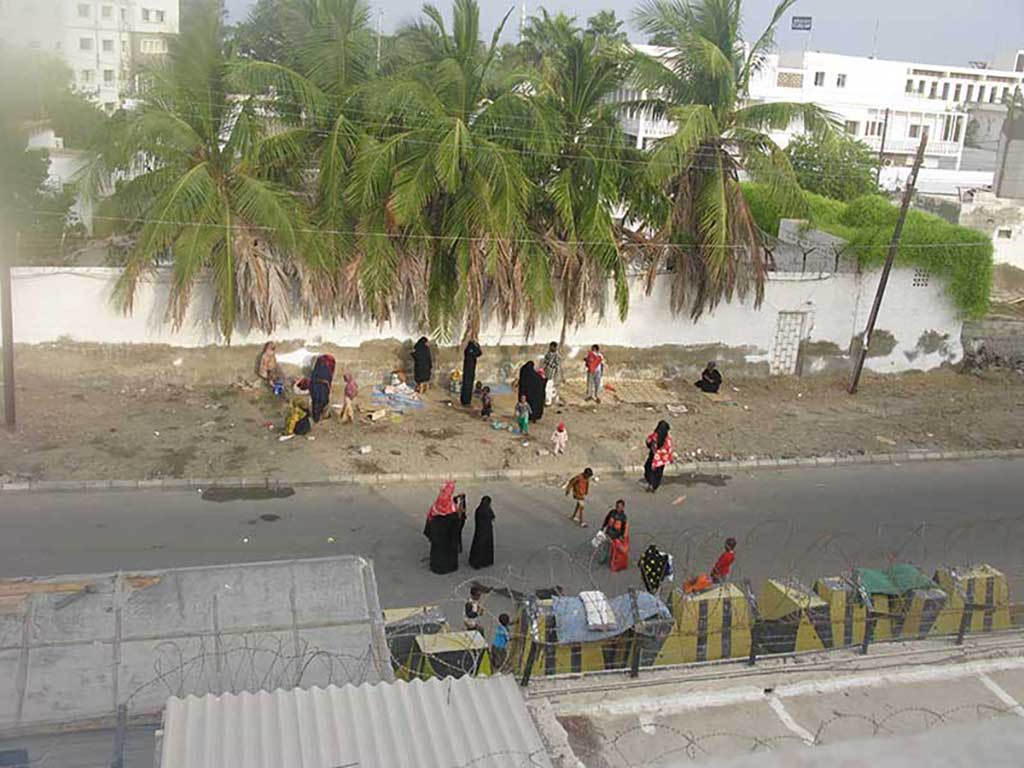 A view of the street as seen from atop a roof; there are men, women and children sitting on blankets.