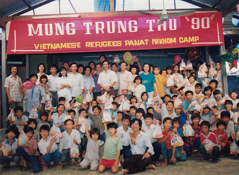 Large group of men, women and children with smiling faces, celebratory balloons and gift bags.