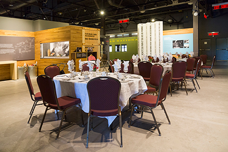 Round dining tables covered in white linen can be seen in an exhibition hall.