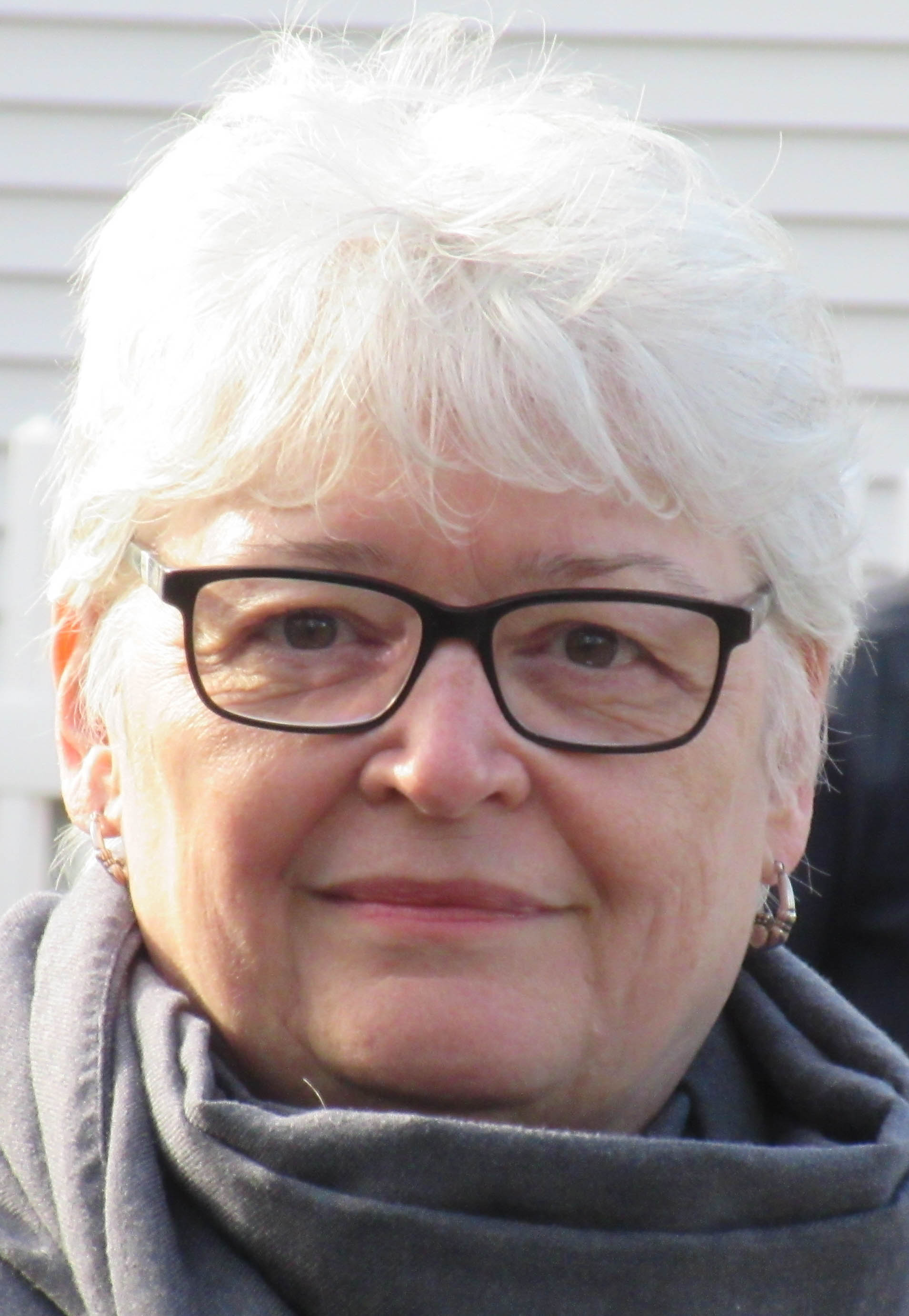 A headshot of a woman with short grey hair and glasses.