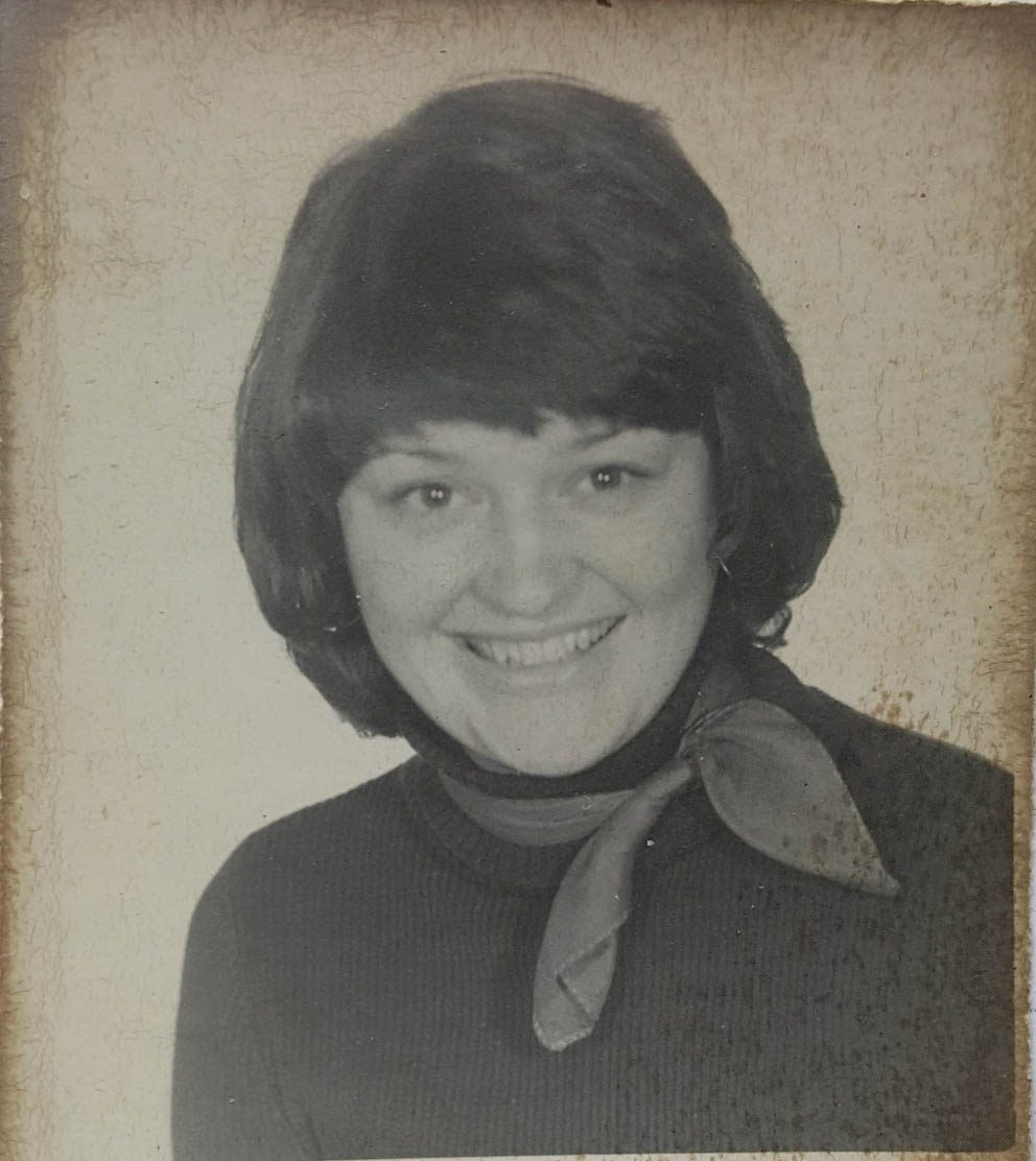 A speckled and stained black and white head and shoulders shot of a woman, smiling.