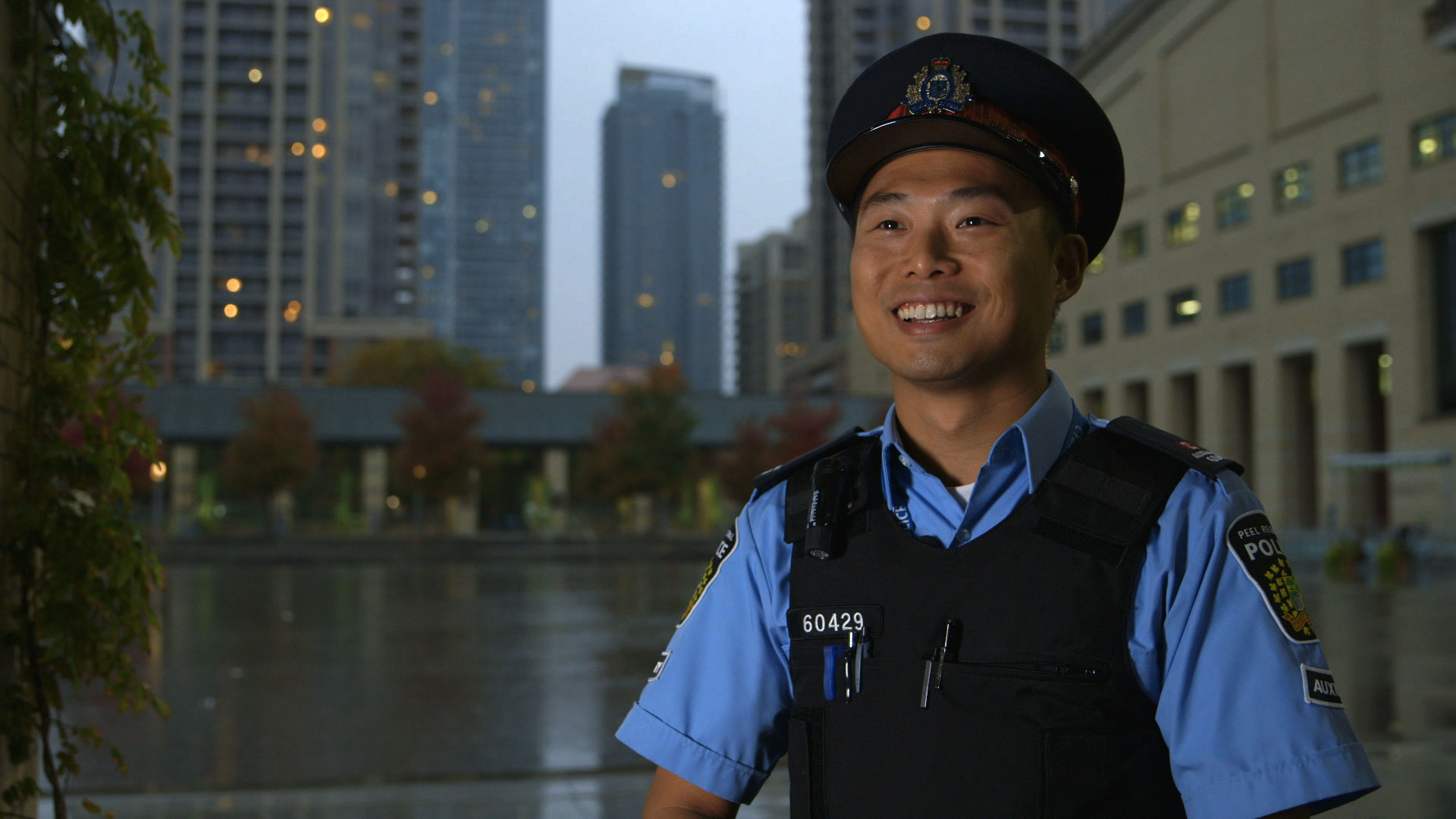 A man in a police uniform, smiling, backgrounded by a city street.