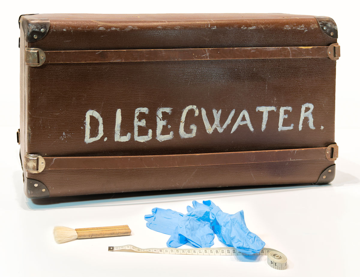 An old suitcase with the name Leegwater painted on it in large letters.