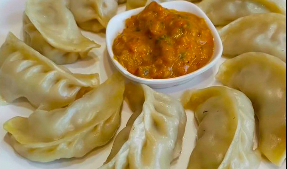 A plate of momo with a ramekin of spicy sauce.