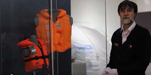A man stands behind a glass case with two lifejackets inside it.