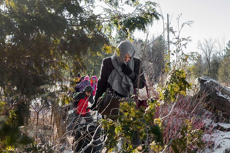 A woman wearing a hijab pulls a suitcase through a wooded area.