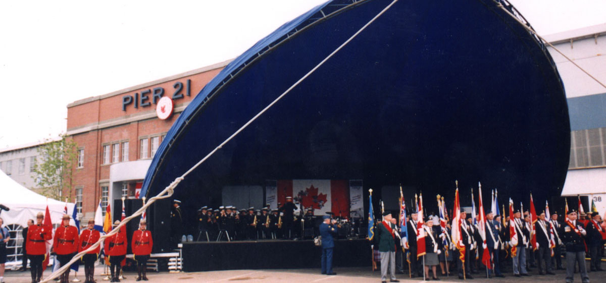 In front of Pier 21, a crowd is gathered under a large awning with a stage.