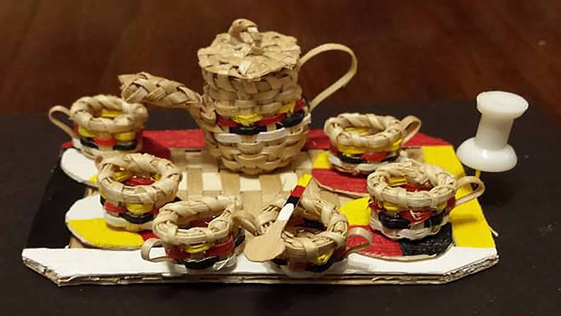 A set of six teacups, each smaller than a pushpin, and a miniature teapot, all woven from wood strips.