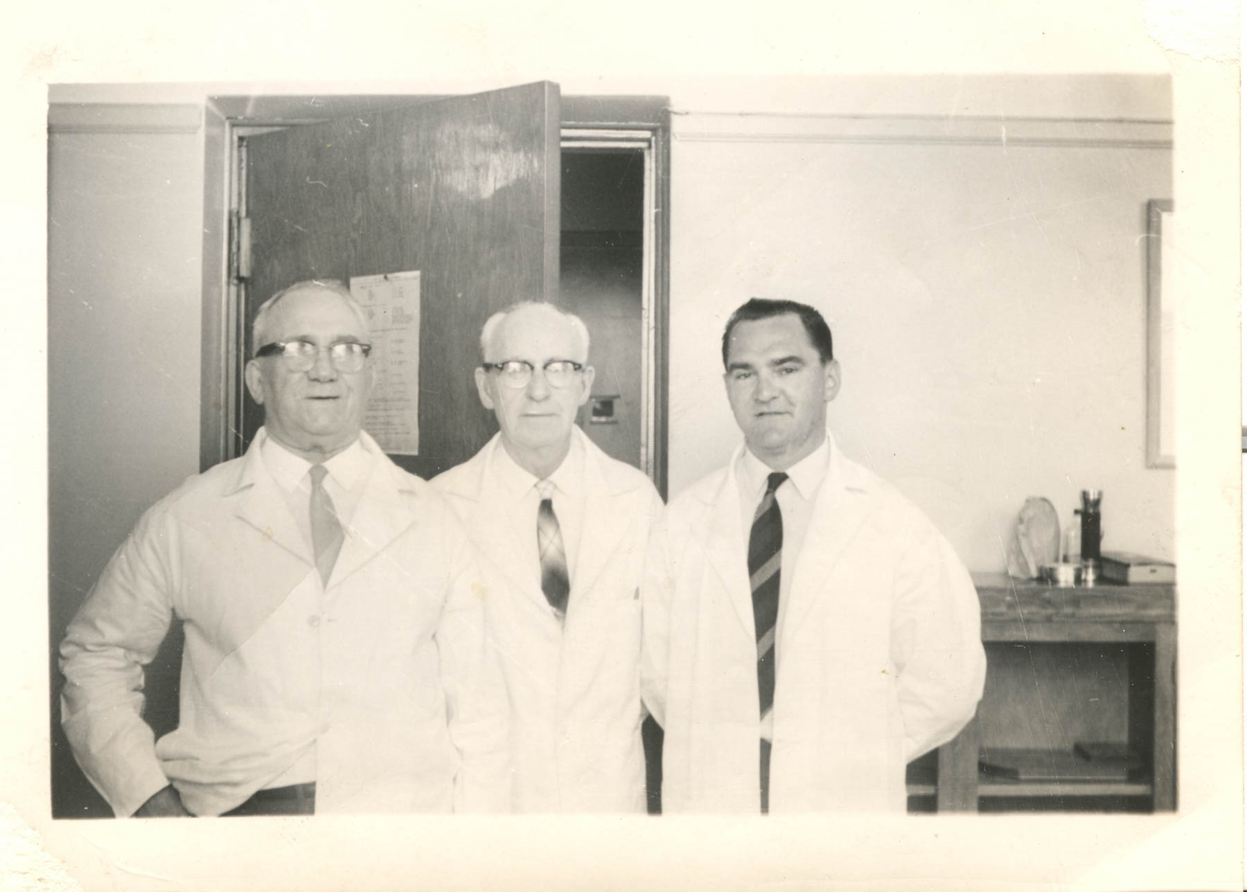 Black and white photo of three white doctors in white coats and neckties.