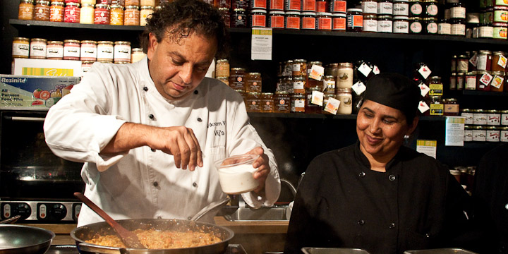 A chef adds salt to a skillet while a sous chef looks on.