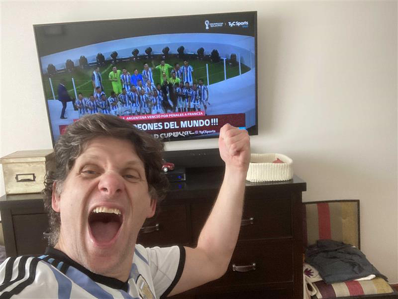 A man cheers in front of a television showing the 2022 world champion Argentinian Soccer team.