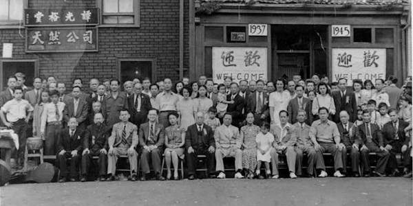 A large group of people pose outside of a building with a banner that says “CHINA-VJ-DAY.”