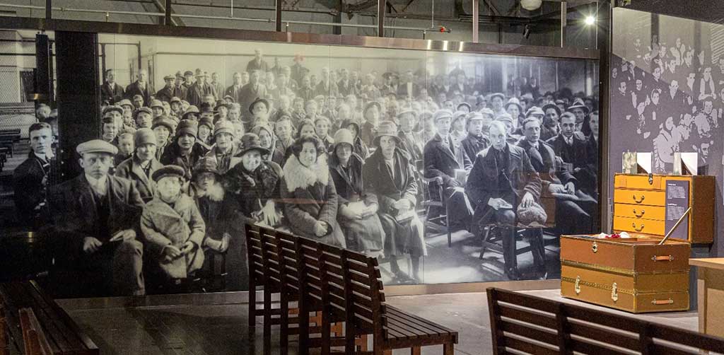 One wall in a section of the museum is decorated with a huge print of an old black and white photograph with white people in a large waiting hall. They all look at the camera.