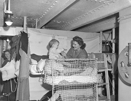 Woman plays with baby on a bunk of an older transport ship.